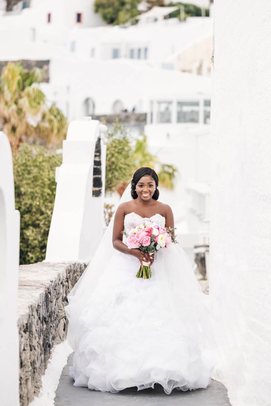 Bride walking with her bouquet in hand against the backdrop of Santorini's stunning views